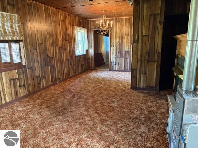 4161 Elbow Lake Rd, Prescott, MI 48756 - unfurnished dining area with a chandelier, wood walls, a fireplace, and carpet