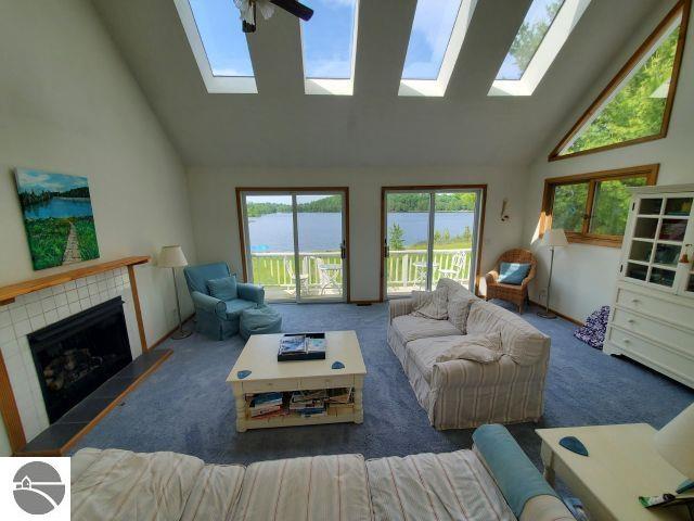 5736 Greenwood Rd, Gladwin, MI 48624 - carpeted living room with a skylight, high vaulted ceiling, healthy amount of natural light, a fireplace, and a water view