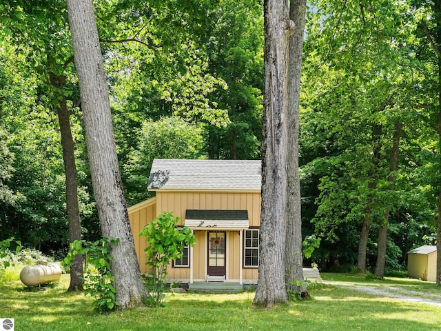 10090 E 48th Rd, Cadillac, MI 49601 - view of front of property featuring a shingled roof, a front yard, an outbuilding, and board and batten siding