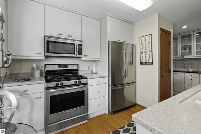 3810 Ridgeway Pl, Traverse City, MI 49684 - kitchen featuring appliances with stainless steel finishes, light wood-style floors, white cabinetry, glass insert cabinets, and tasteful backsplash