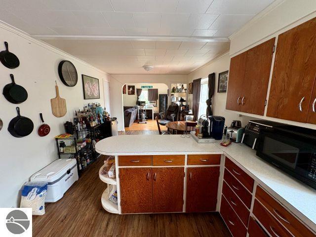 180 S Benzie Blvd, Beulah, MI 49617 - kitchen featuring black microwave, a peninsula, light countertops, dark wood-style floors, and crown molding