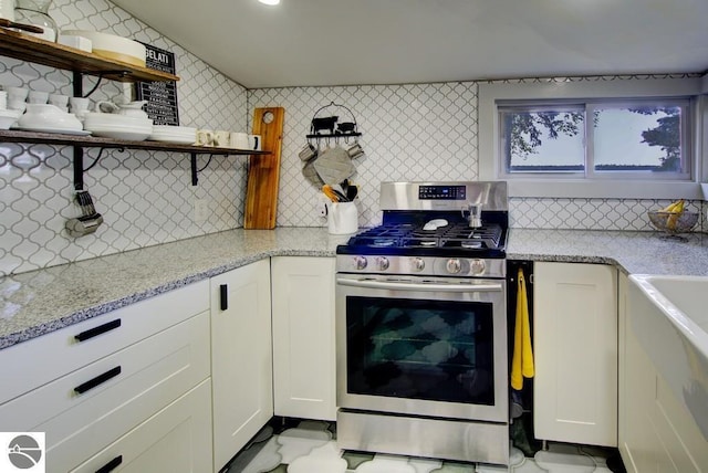 7600 Maple St, Grawn, MI 49637 - kitchen with stainless steel gas stove, open shelves, backsplash, white cabinets, and light stone counters