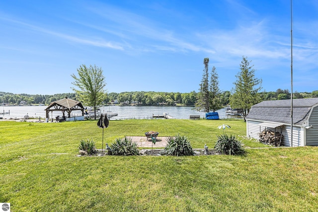 8781 Clam Lake Rd, Bellaire, MI 49615 - view of grassy yard featuring a gazebo, a water view, a storage shed, and a fire pit