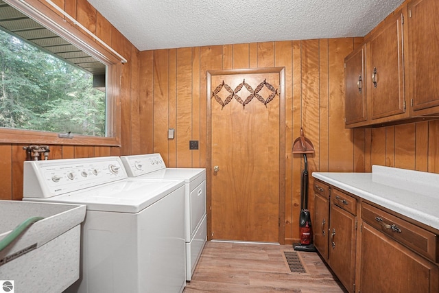 10085 Harmony Dr, Interlochen, MI 49643 - washroom featuring independent washer and dryer, light wood-style flooring, a textured ceiling, cabinet space, and wooden walls
