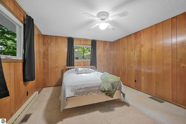 10085 Harmony Dr, Interlochen, MI 49643 - carpeted bedroom featuring wooden walls, baseboard heating, a textured ceiling, and ceiling fan
