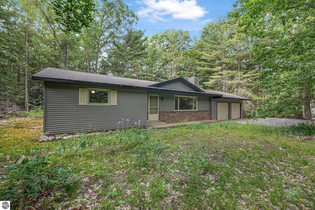 10085 Harmony Dr, Interlochen, MI 49643 - view of front of property featuring a chimney, an attached garage, brick siding, and driveway