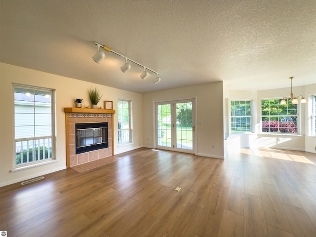 318 Red Maple Ln, Shepherd, MI 48883 - unfurnished living room featuring a tiled fireplace, track lighting, wood finished floors, a textured ceiling, and a chandelier