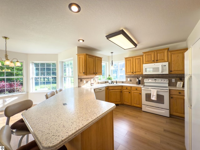 318 Red Maple Ln, Shepherd, MI 48883 - kitchen featuring white appliances, a peninsula, backsplash, a kitchen breakfast bar, and hanging light fixtures