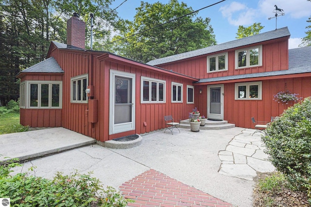7822 W Welch Rd, Empire, MI 49630 - back of property with board and batten siding, a patio area, a chimney, and roof with shingles