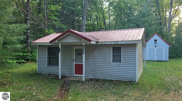 1947 NE Anita Rd, Kalkaska, MI 49646 - bungalow-style house featuring a metal roof, an outdoor structure, a forest view, and a front lawn