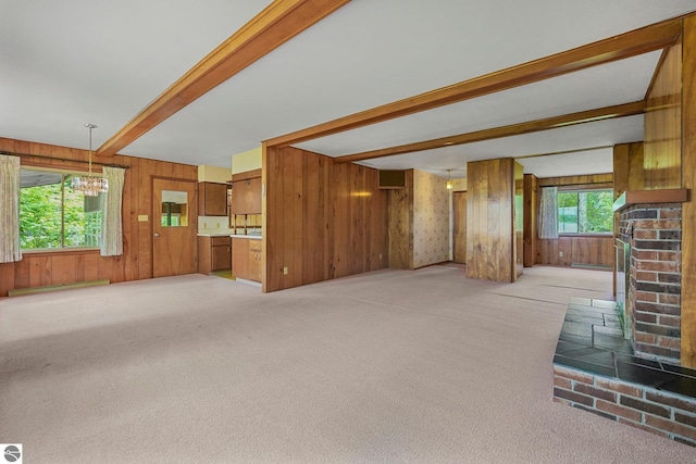 7786 N Shore Ct, Grawn, MI 49637 - unfurnished living room with beamed ceiling, a chandelier, light colored carpet, wooden walls, and a fireplace