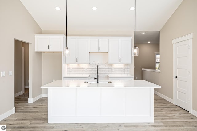1572 Oban Way, Traverse City, MI 49696 - kitchen featuring a center island with sink, backsplash, lofted ceiling, white cabinets, and light wood-style flooring