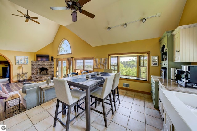 10702 E Hill Top Rd, Suttons Bay, MI 49682 - dining area with a ceiling fan, a fireplace, high vaulted ceiling, track lighting, and light tile patterned floors