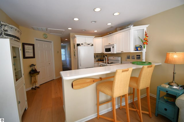 13354 Stover Rd Unit 6, Charlevoix, MI 49720 - kitchen with white appliances, a peninsula, white cabinetry, recessed lighting, and light wood-type flooring