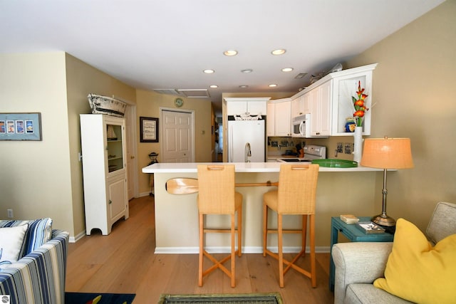13354 Stover Rd Unit 6, Charlevoix, MI 49720 - kitchen with white appliances, a peninsula, light wood-style floors, recessed lighting, and white cabinetry