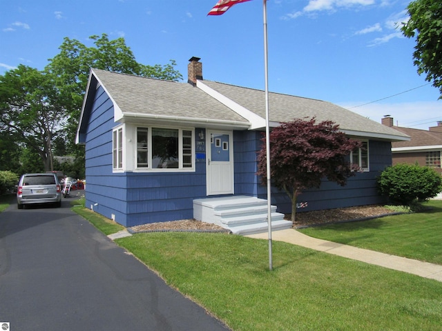 705 E Bay St, East Tawas, MI 48730 - view of front of property featuring roof with shingles, a chimney, and a front lawn
