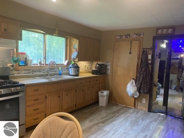 802 W 4th Rd, Buckley, MI 49620 - kitchen featuring stainless steel range with gas stovetop, light wood-style floors, light countertops, backsplash, and wall chimney exhaust hood