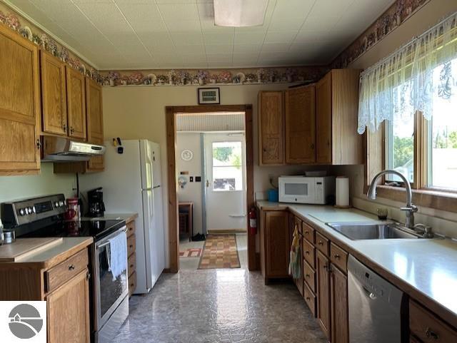 2393 Oates Rd, Tawas City, MI 48763 - kitchen with appliances with stainless steel finishes, under cabinet range hood, light countertops, brown cabinetry, and light flooring