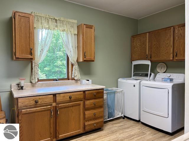 2393 Oates Rd, Tawas City, MI 48763 - laundry area with cabinet space, washing machine and clothes dryer, and light wood-style floors