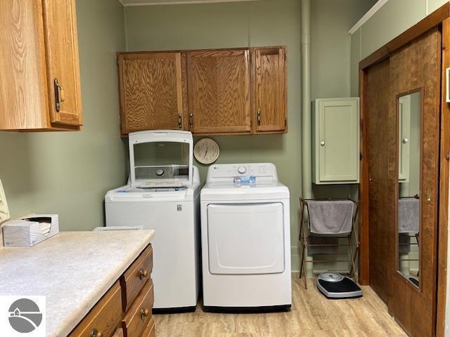 2393 Oates Rd, Tawas City, MI 48763 - washroom with cabinet space, light wood-type flooring, and separate washer and dryer