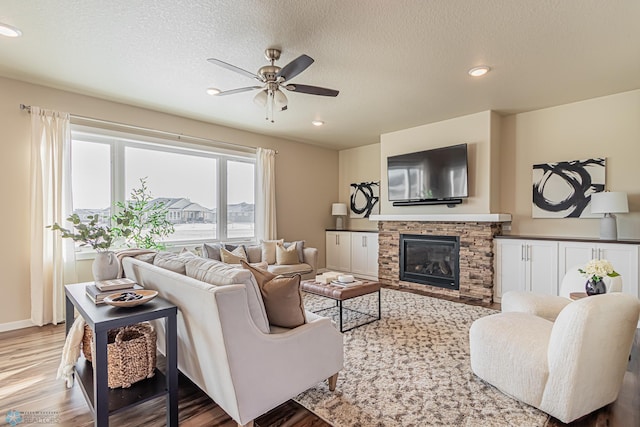 living room with a textured ceiling, a fireplace, wood-type flooring, and ceiling fan