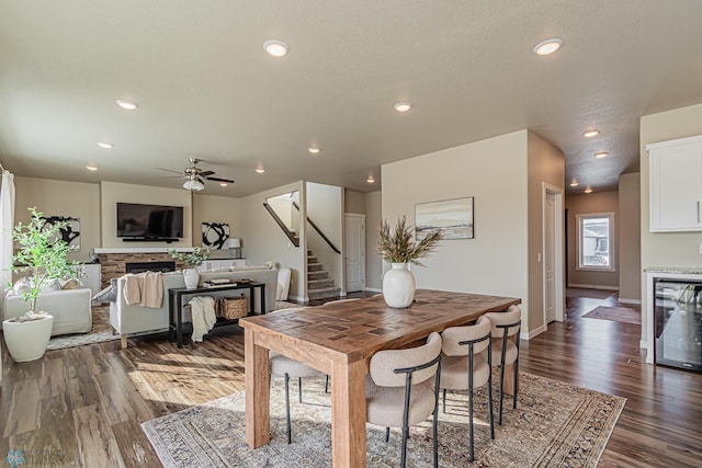 dining area featuring wine cooler, dark hardwood / wood-style flooring, ceiling fan, and a fireplace