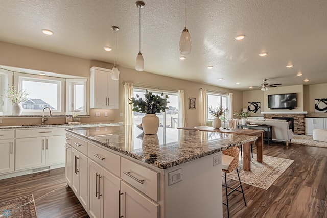 kitchen with dark hardwood / wood-style floors, a stone fireplace, hanging light fixtures, a center island, and white cabinetry