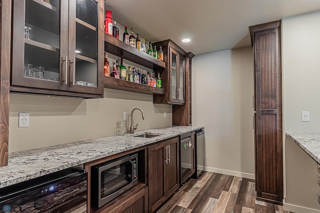 bar with sink, light stone countertops, dark wood-type flooring, and dark brown cabinetry