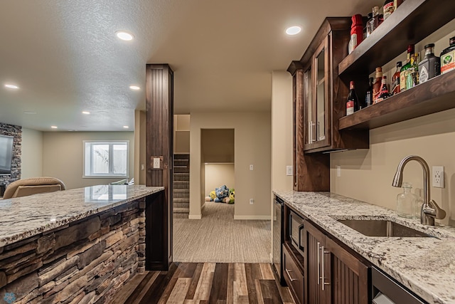 kitchen with dark brown cabinets, light stone countertops, dark carpet, a textured ceiling, and sink