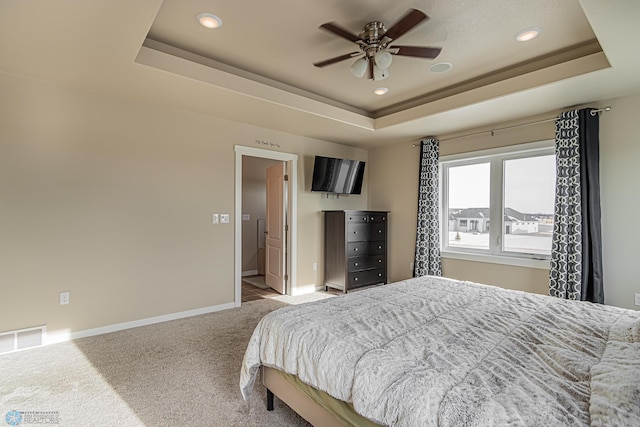 bedroom with a tray ceiling, carpet flooring, ensuite bathroom, and ceiling fan