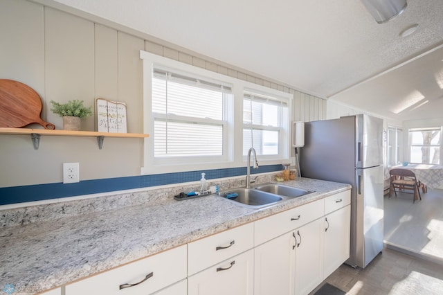 kitchen with a wealth of natural light, stainless steel fridge, white cabinets, and sink