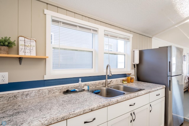 kitchen featuring white cabinets, light stone countertops, stainless steel refrigerator, sink, and a textured ceiling