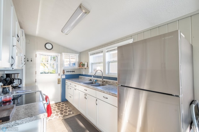 kitchen with stainless steel refrigerator, vaulted ceiling, white cabinets, and sink