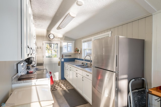 kitchen with white cabinetry, sink, stainless steel fridge, a textured ceiling, and lofted ceiling