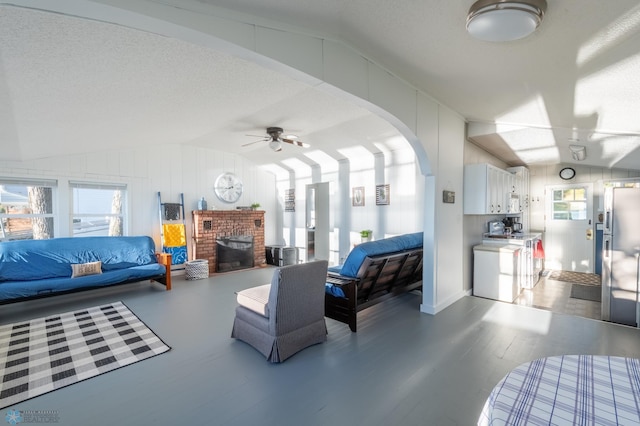 living room featuring ceiling fan, a brick fireplace, a textured ceiling, hardwood / wood-style floors, and lofted ceiling