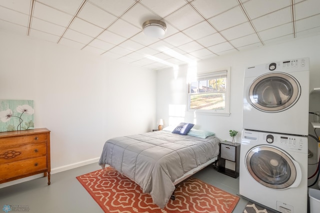 bedroom with concrete flooring, a drop ceiling, and stacked washer and clothes dryer