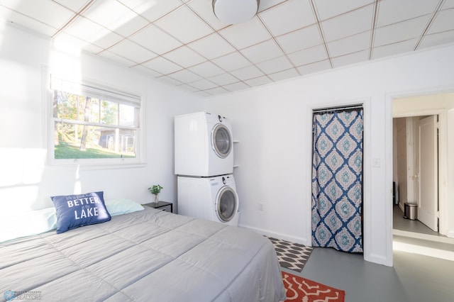 bedroom featuring concrete floors, a paneled ceiling, and stacked washing maching and dryer