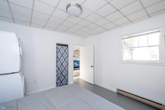 unfurnished bedroom featuring a drop ceiling, stacked washer / dryer, and a baseboard heating unit