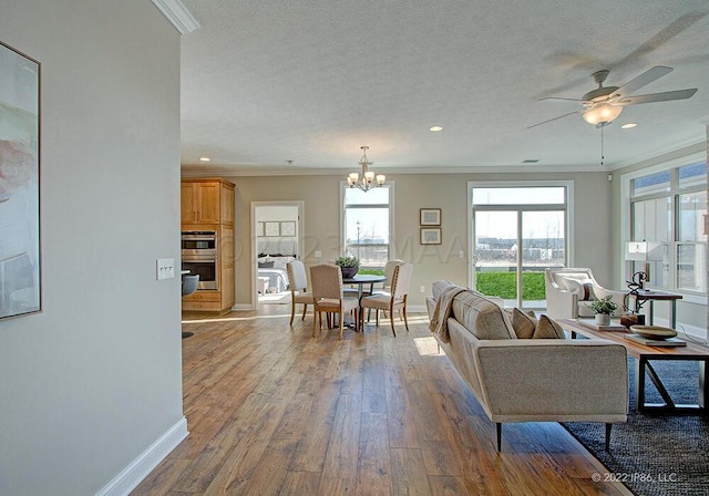 living room featuring hardwood / wood-style flooring, ornamental molding, ceiling fan with notable chandelier, and a textured ceiling