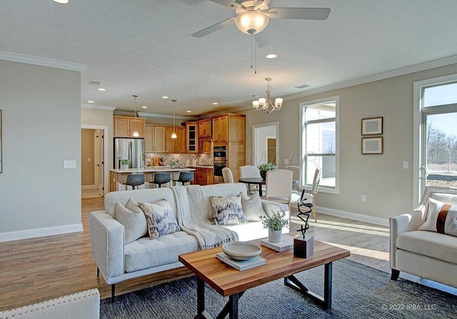 living room with ceiling fan with notable chandelier, a textured ceiling, hardwood / wood-style floors, and crown molding