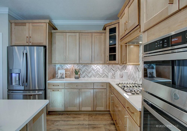 kitchen featuring appliances with stainless steel finishes, light brown cabinets, tasteful backsplash, crown molding, and hardwood / wood-style flooring