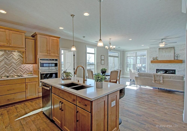 kitchen featuring pendant lighting, wood-type flooring, stainless steel appliances, sink, and a stone fireplace