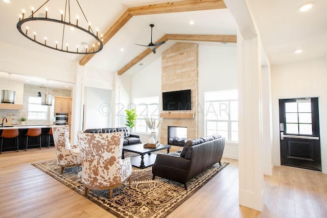 living room featuring beamed ceiling, a multi sided fireplace, high vaulted ceiling, ceiling fan with notable chandelier, and light hardwood / wood-style flooring