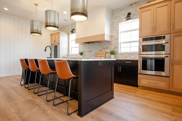 kitchen featuring stainless steel double oven, light hardwood / wood-style floors, a kitchen island with sink, and plenty of natural light