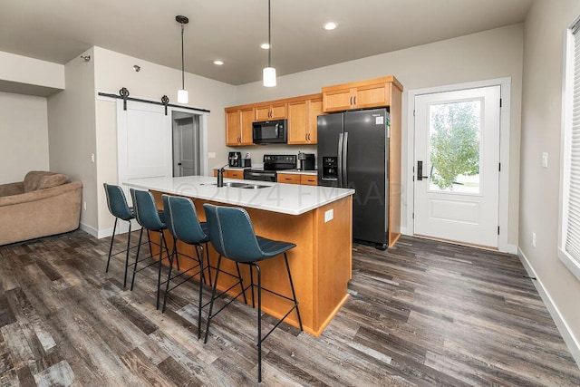 kitchen with a barn door, hanging light fixtures, black appliances, dark wood-type flooring, and an island with sink