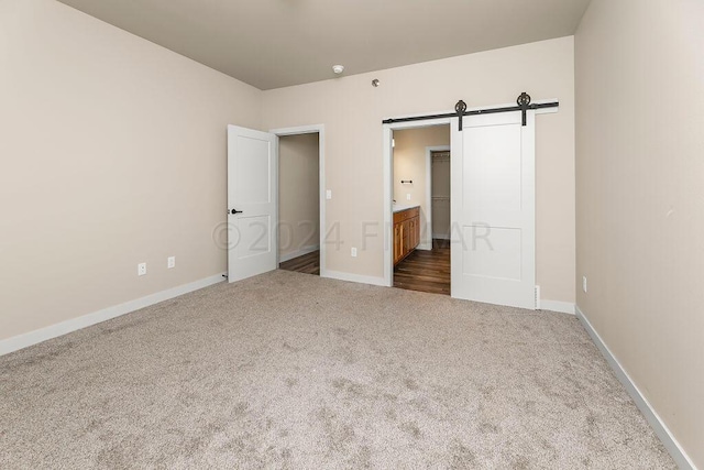 unfurnished bedroom with connected bathroom, a barn door, and carpet floors