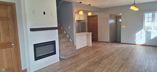 kitchen featuring white cabinets, pendant lighting, hardwood / wood-style flooring, stainless steel fridge, and a large fireplace