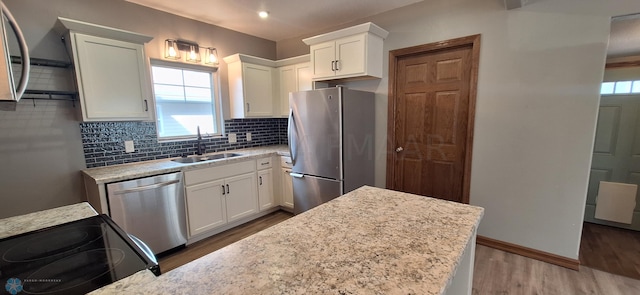 kitchen with white cabinetry, stainless steel appliances, decorative backsplash, wood-type flooring, and sink