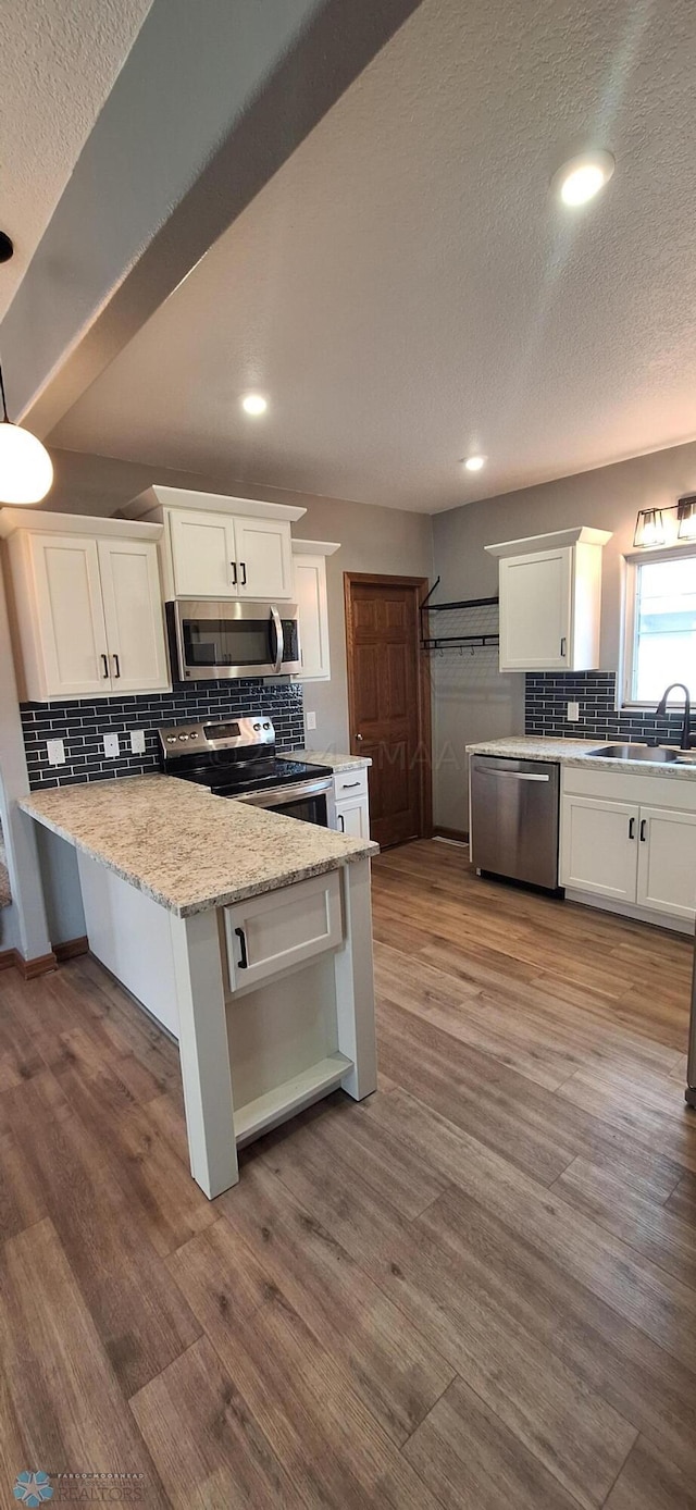 kitchen with white cabinetry, hardwood / wood-style flooring, stainless steel appliances, and light stone counters