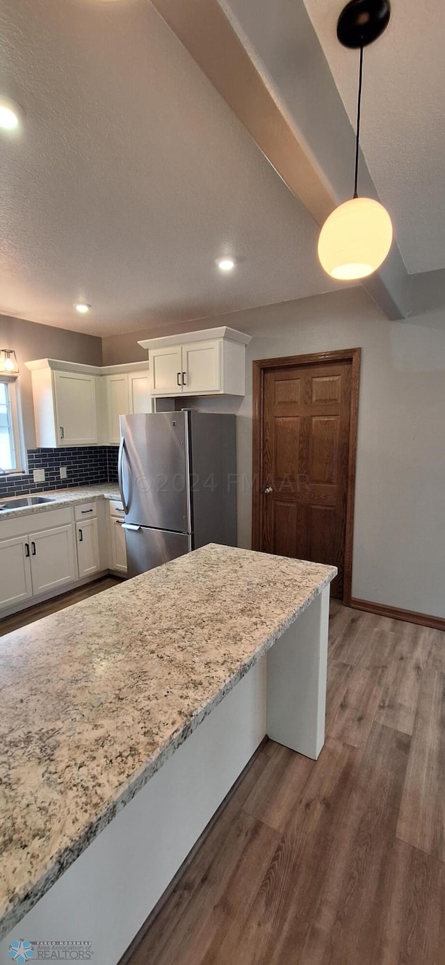 kitchen with wood-type flooring, hanging light fixtures, white cabinets, light stone counters, and stainless steel refrigerator